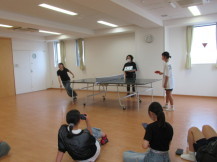 卓球勝負をする2人の男の子と観戦している女の子たちの写真