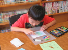 カラフルなパステルを使ってポストカードに色を付けている男の子の写真