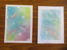 青、黄色、ピンクのグラデーションの中にイルカが描かれているポストカードの作品2点の写真