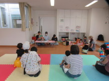 絵本の読み聞かせを床に座って聞いている数組の親子の写真