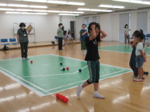 床に緑色のシートを広げてその上にボールを置いてボッチャを楽しむ参加者の写真