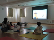 暗くした部屋の前方に設置されたスクリーンに映し出された映画を見ている親子の写真