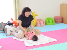 仰向けになった乳幼児の手を持ってマッサージしている笑顔の母親の写真