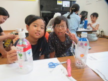 完成した作品を机の上に置いてピースサインで撮影している2人の女の子の写真