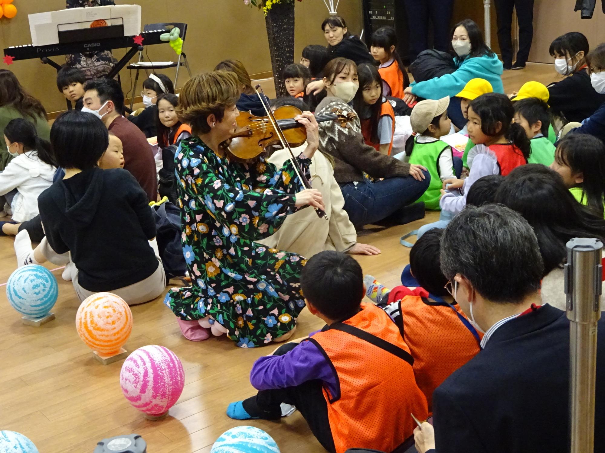 座っている参加者の近くに来てヴァイオリンの演奏を披露する大谷康子氏の写真とその演奏を聞く参加者の写真