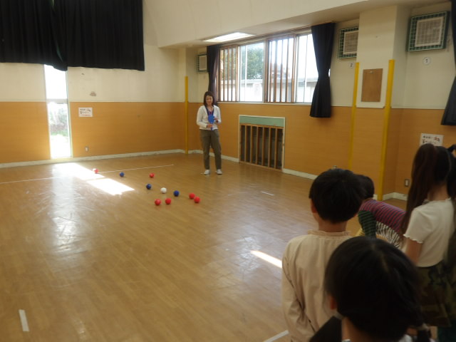 手前に子供達、奥に審判をしている職員と子供達が投げたボールがある写真