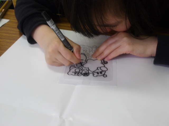 プラバンの上からイラストをペンでなぞる小学生の写真