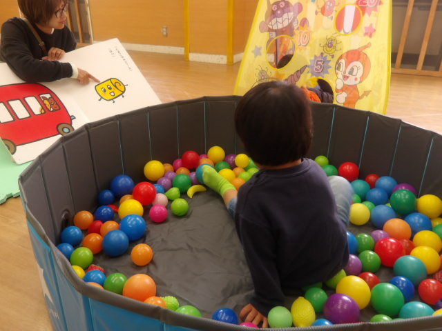 ボールプールに入ってママの読み聞かせを聞いている幼児の写真