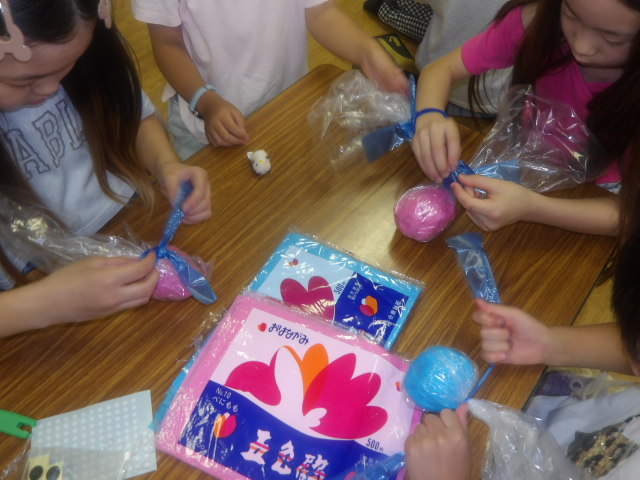 てるてるぼうずに使うスズランテープを結ぶ小学生達の写真