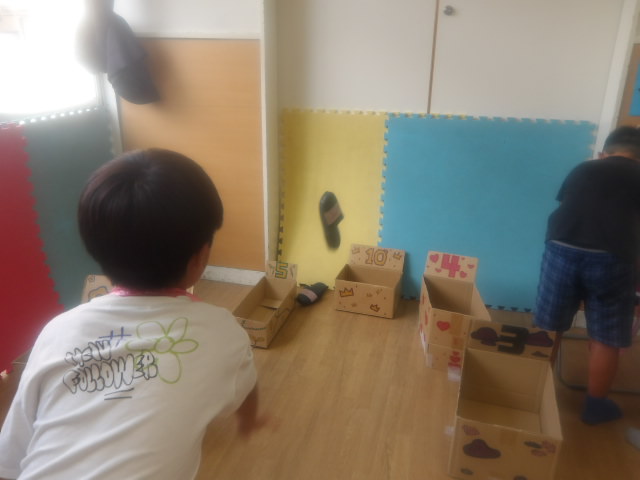 段ボールで作った的入れにスリッパを投げ入れる子どもの写真