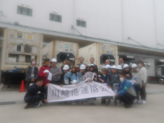 「川崎港運協会」と書かれているのぼりを持っている川崎港の職員と集合写真を撮る子供達の写真。