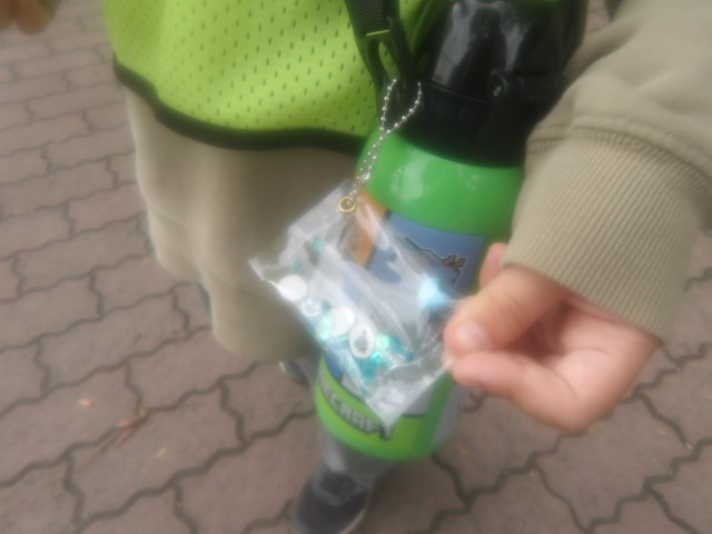 透明のテーブルクロスで作った入れ物の中にビーズ小さいプラバンが入ったキーホルダーを持つ子供の手の写真