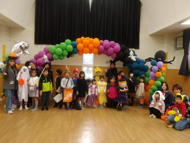 集会室内にあるバルーンアーチの下で集合写真を撮る仮装した子供達の写真