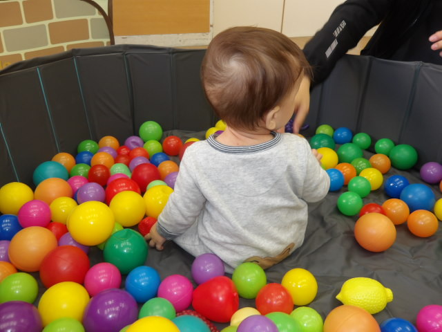 ボールプールの中に入り、様々なカラーボールを見る乳幼児の写真