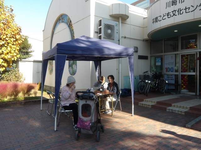 こども文化センター前に設置したテントの下に、椅子に座りながらコーヒーやお菓子を楽しむ地域住民の写真