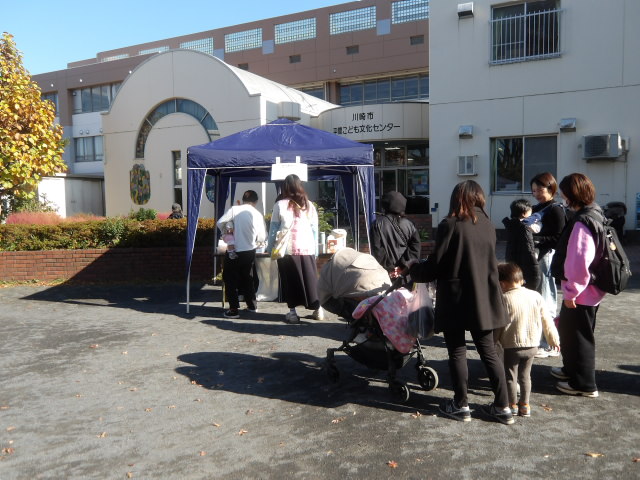平間商店街のお菓子やコーヒーを販売しているテントに並ぶ幼児親子や地域住民の写真