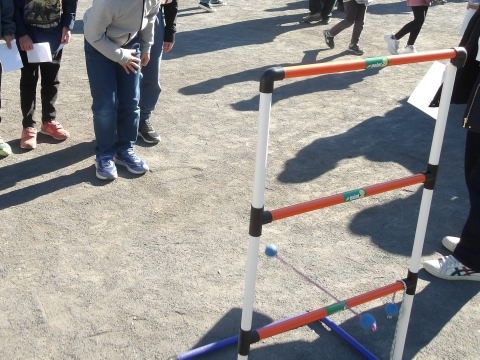 プラスチックの柵に紐にボールが付いたものを投げるゲームラダーゲッターに挑戦する小学生の写真