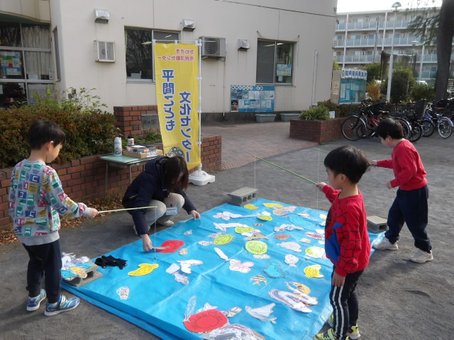 ブルーシートに置いた画用紙に描き、クリップがついた魚を磁石を使って釣る幼児達の写真