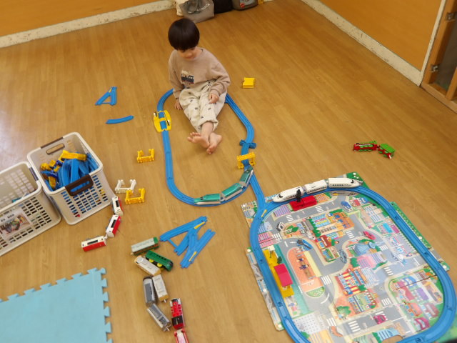 プラレールの線路を繋げて大きい線路を作っている幼児の写真