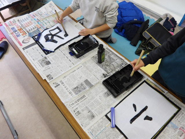 墨のついた筆で半紙に字を書く小学生2人の写真