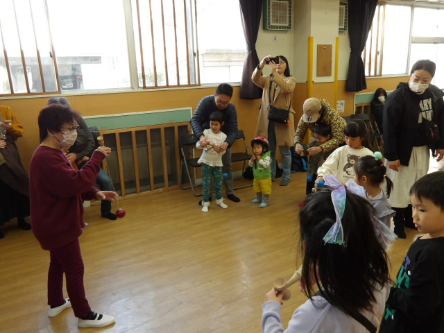 集会室にて、けん玉の先生にけん玉を教わりながら挑戦する参加者達の写真