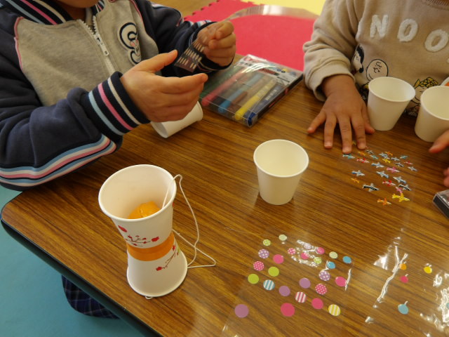 けん玉工作で使う紙コップにシールを貼ろうとする姉妹の幼児の写真