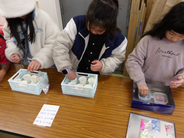 学習室にて、クリアケースの中に様々な大きさのビーズやパーツを入れる小学生達の写真