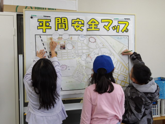 学習室にあるホワイトボードに貼った安全マップに色鉛筆で色を塗る小学生3人の写真