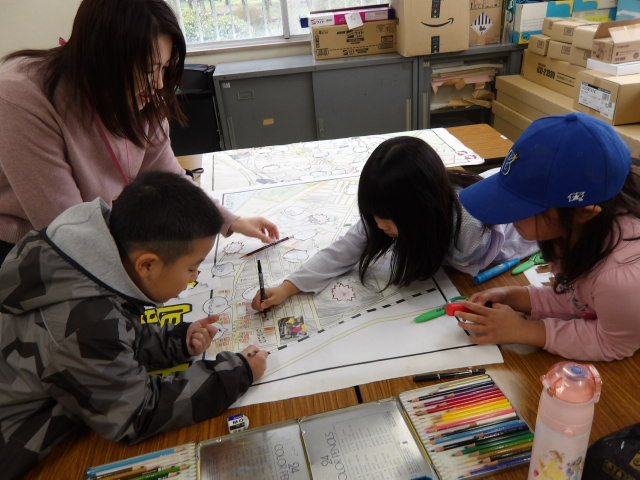 平間安全マップに色を塗る小学生3人と様子を見る子ども達のサポートをする職員の写真