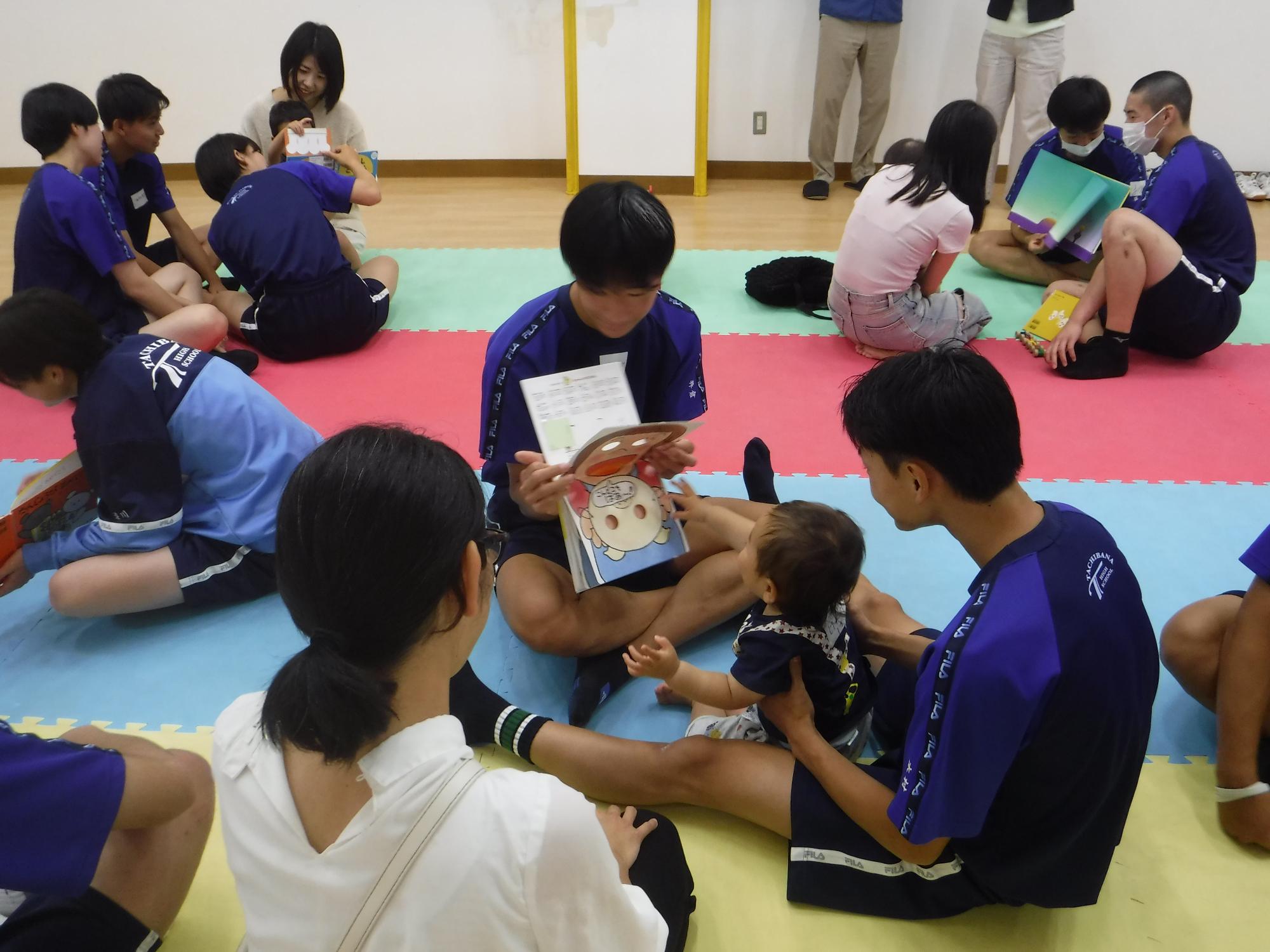 高校生が乳幼児に絵本の読み聞かせをしている写真