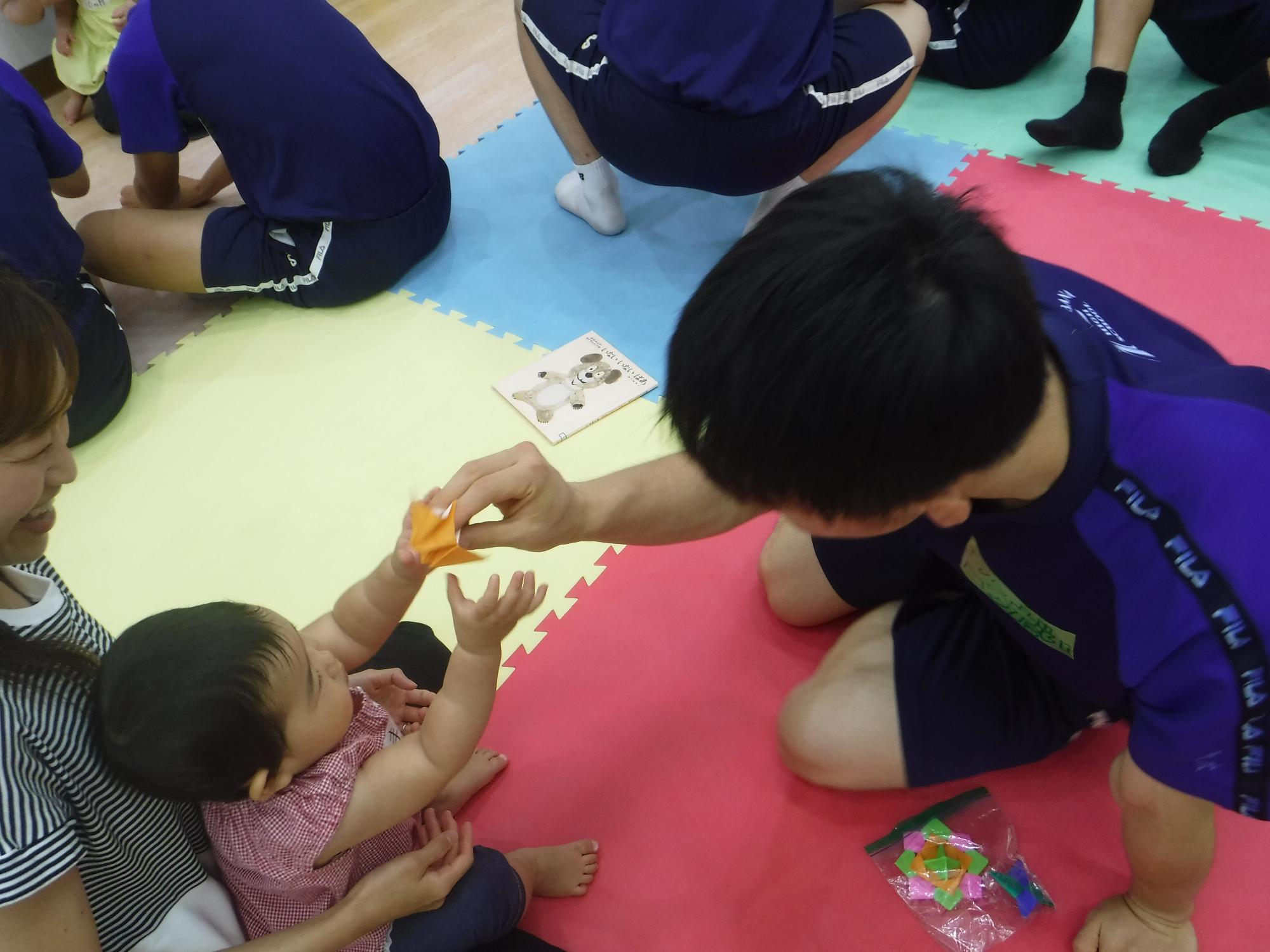 高校生が乳幼児に折り紙を渡している写真