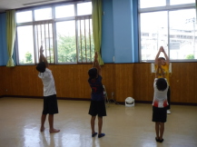 子供たちが組んだ手を頭の上まで持ち上げて、ストレッチをしている写真