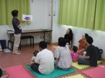 ジョイントマットに座っている幼児親子が読み聞かせを聞いている写真