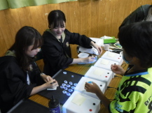 講師の方2人が座って紙に書きこんでいるところを子供が立って見ている写真