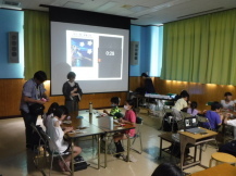 スクリーンを見ながら長机に座って子供たちが工作している会場全体の写真