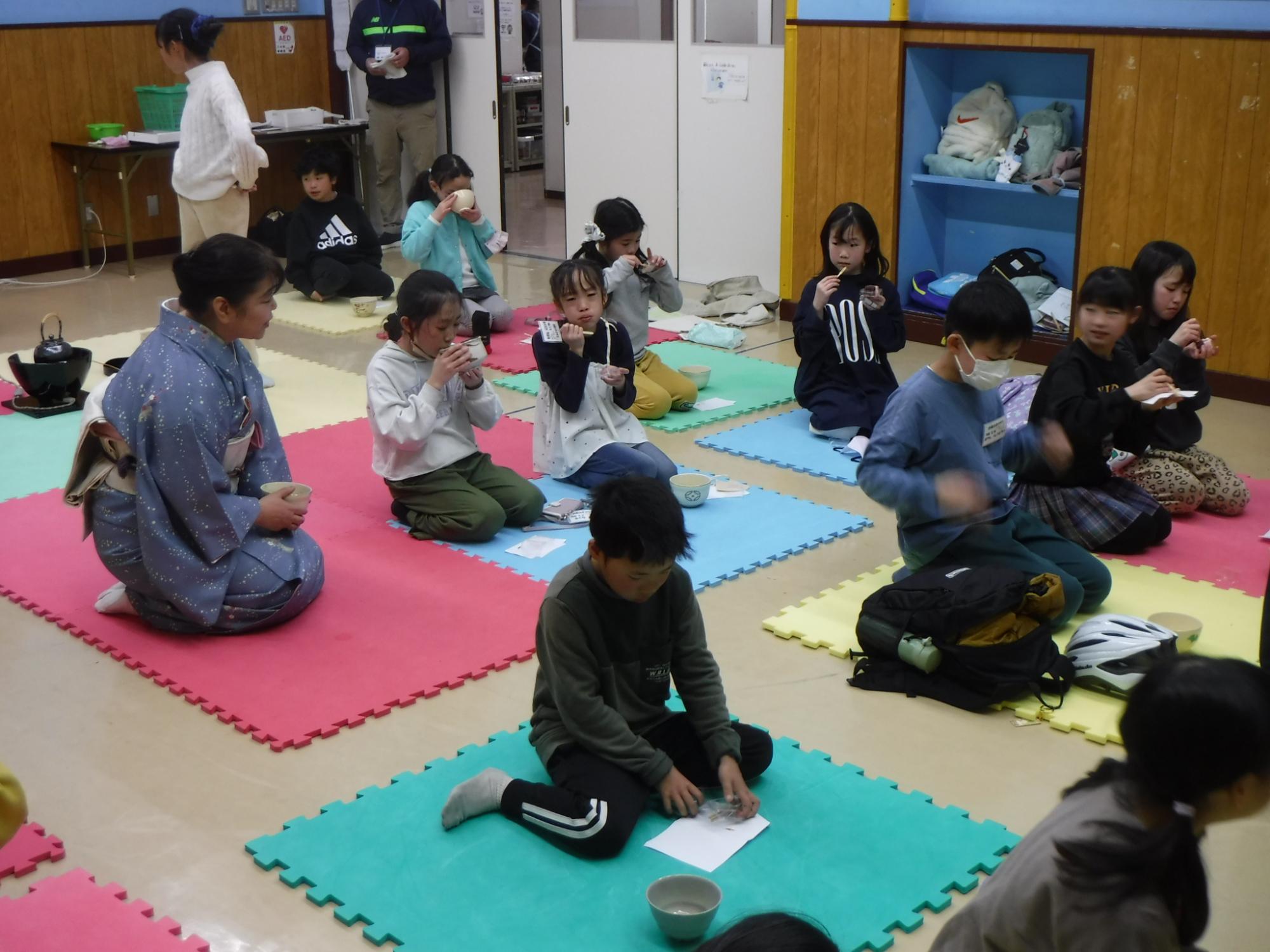 正座して座り、お茶と一緒に和菓子を食べている子供たちの写真
