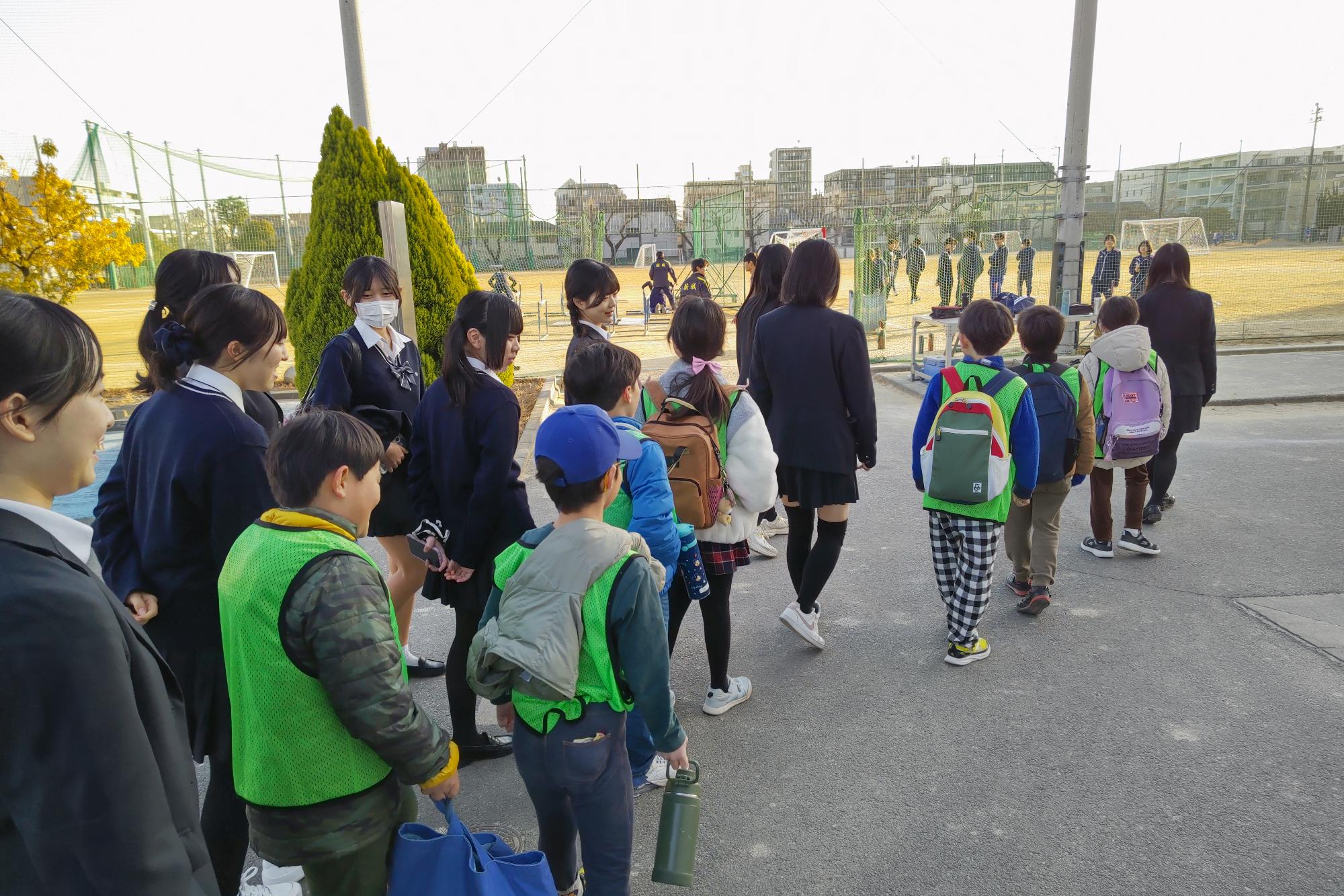 陸上部が活動する高校の校庭を列になって見学する子どもたち