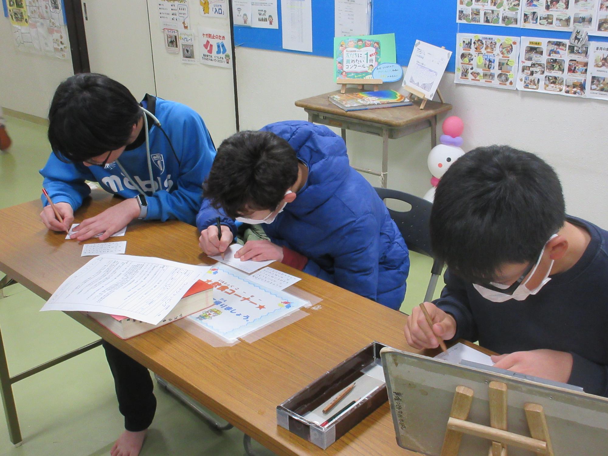 長テーブルに座りあいうえお表を見て単語を作る子どもたち