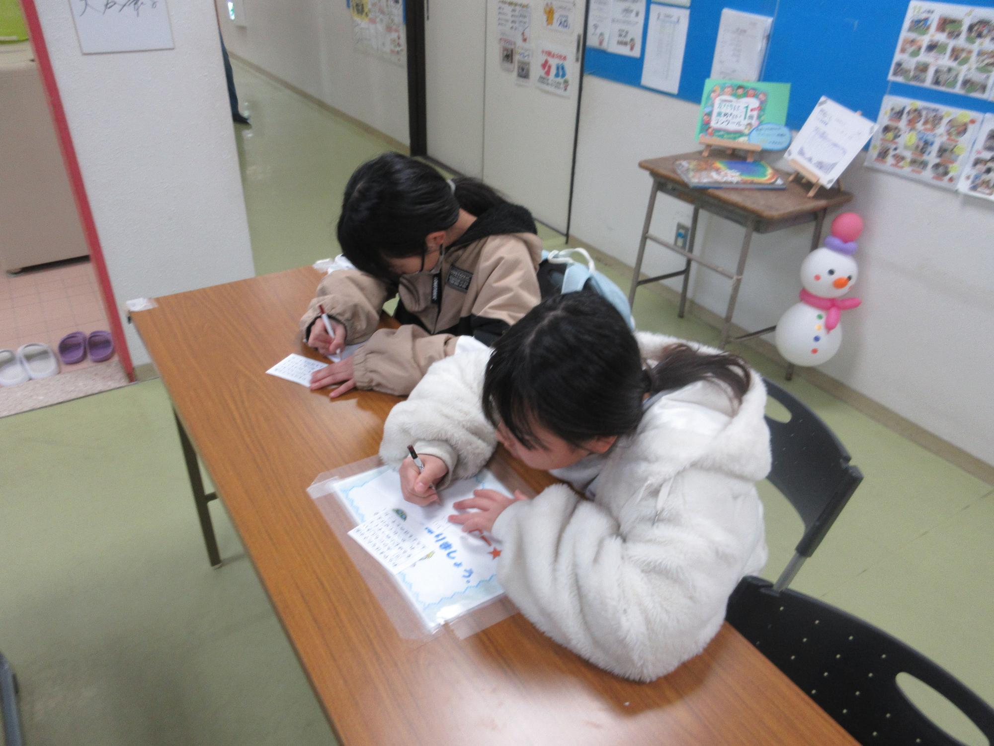 長テーブルに座りあいうえお表を見て単語を作る子ども