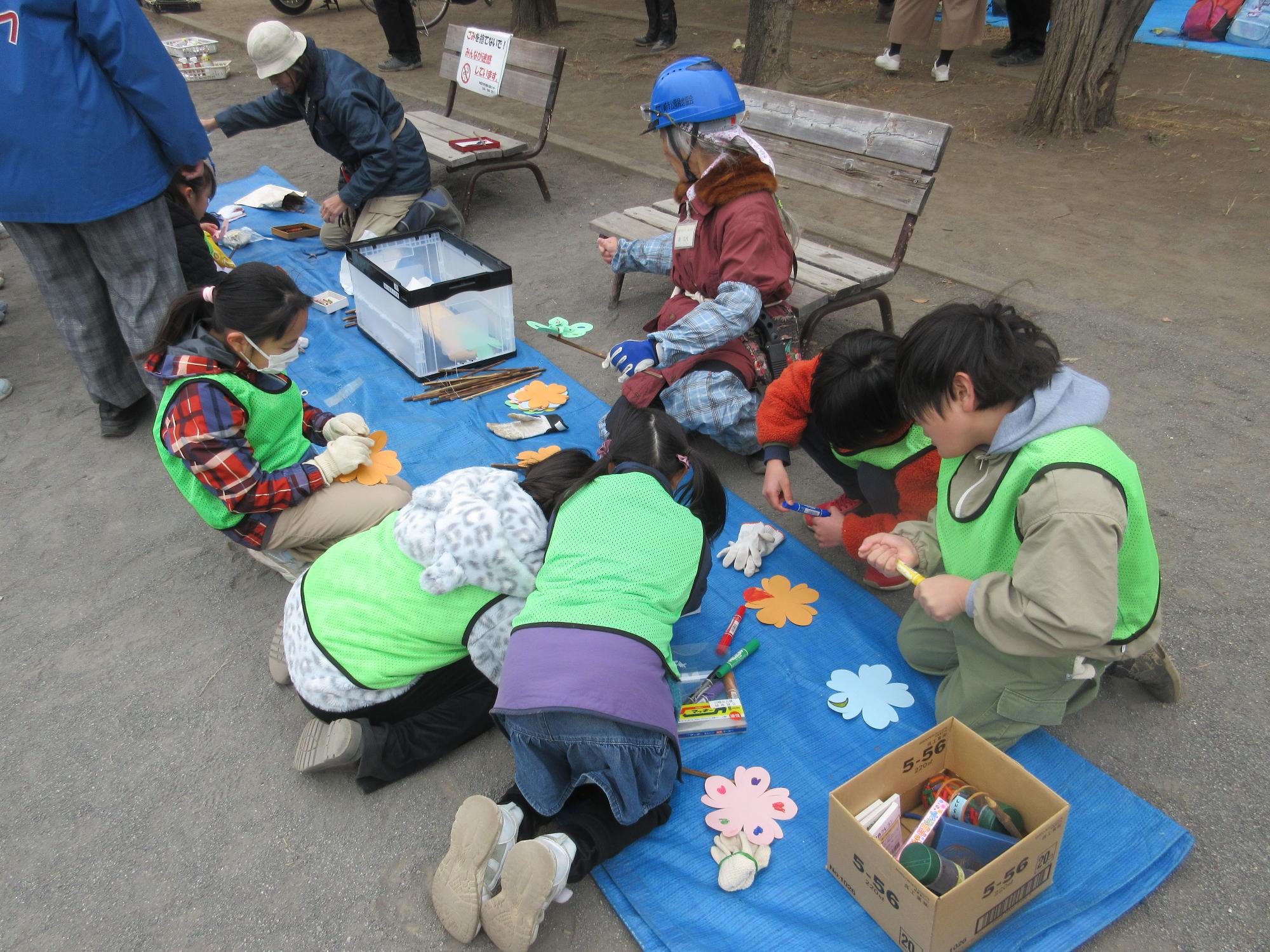公園でブルーシートを広げたところで風車の工作を公園緑地協会の方に教わっている子どもたち