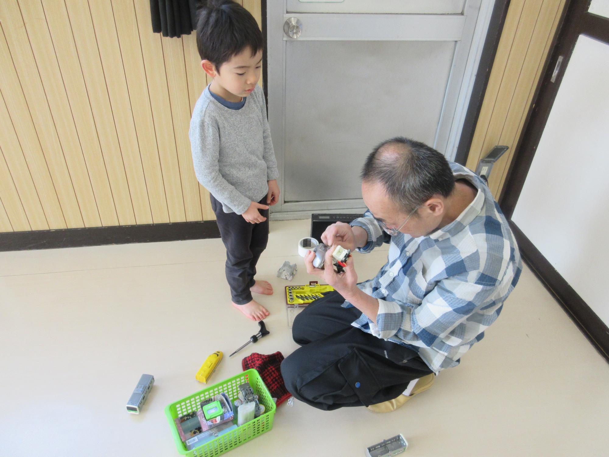 プラレールの車両を修理する職員を見つめるこども