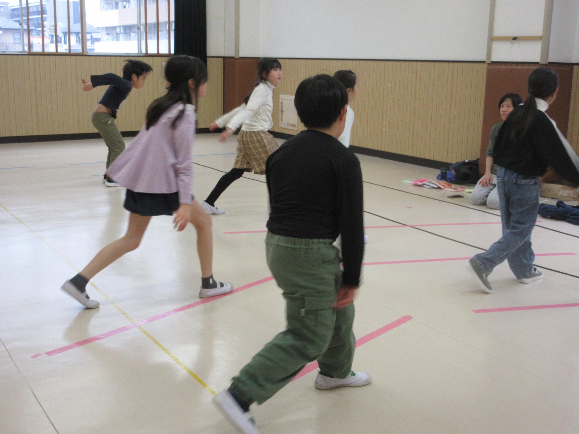 両手を下げて足を前後に開き少し沈み込むステップをするこどもたち