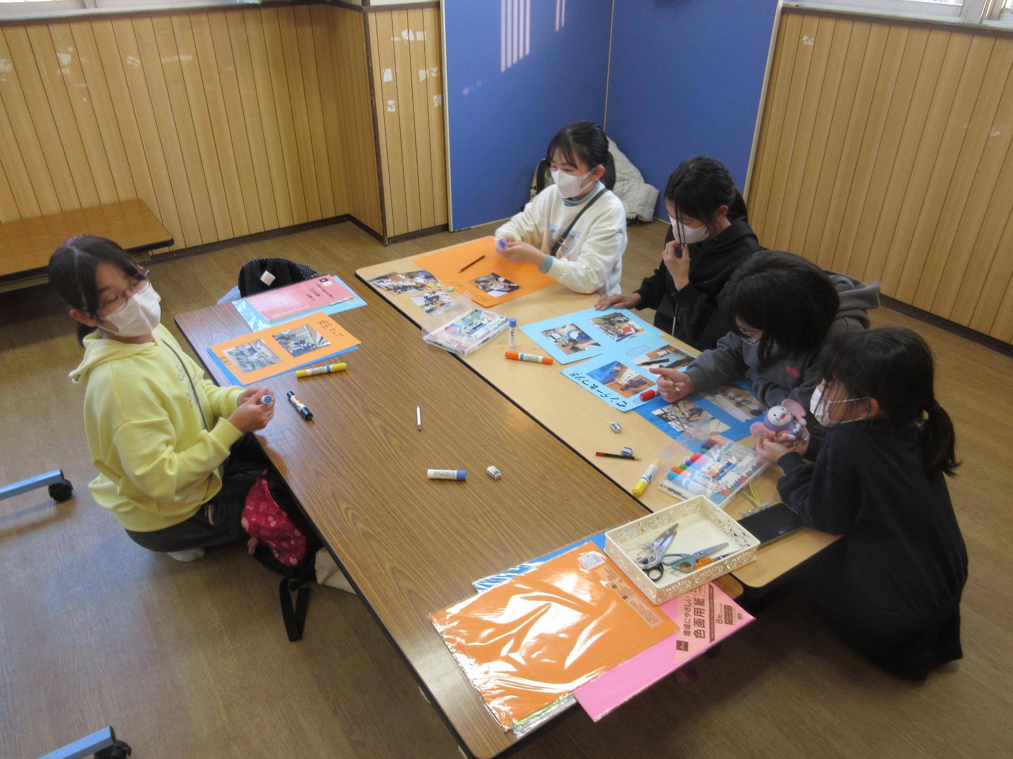 テーブルを囲み画用紙に写真を貼り活動のコメントを書く子どもたち