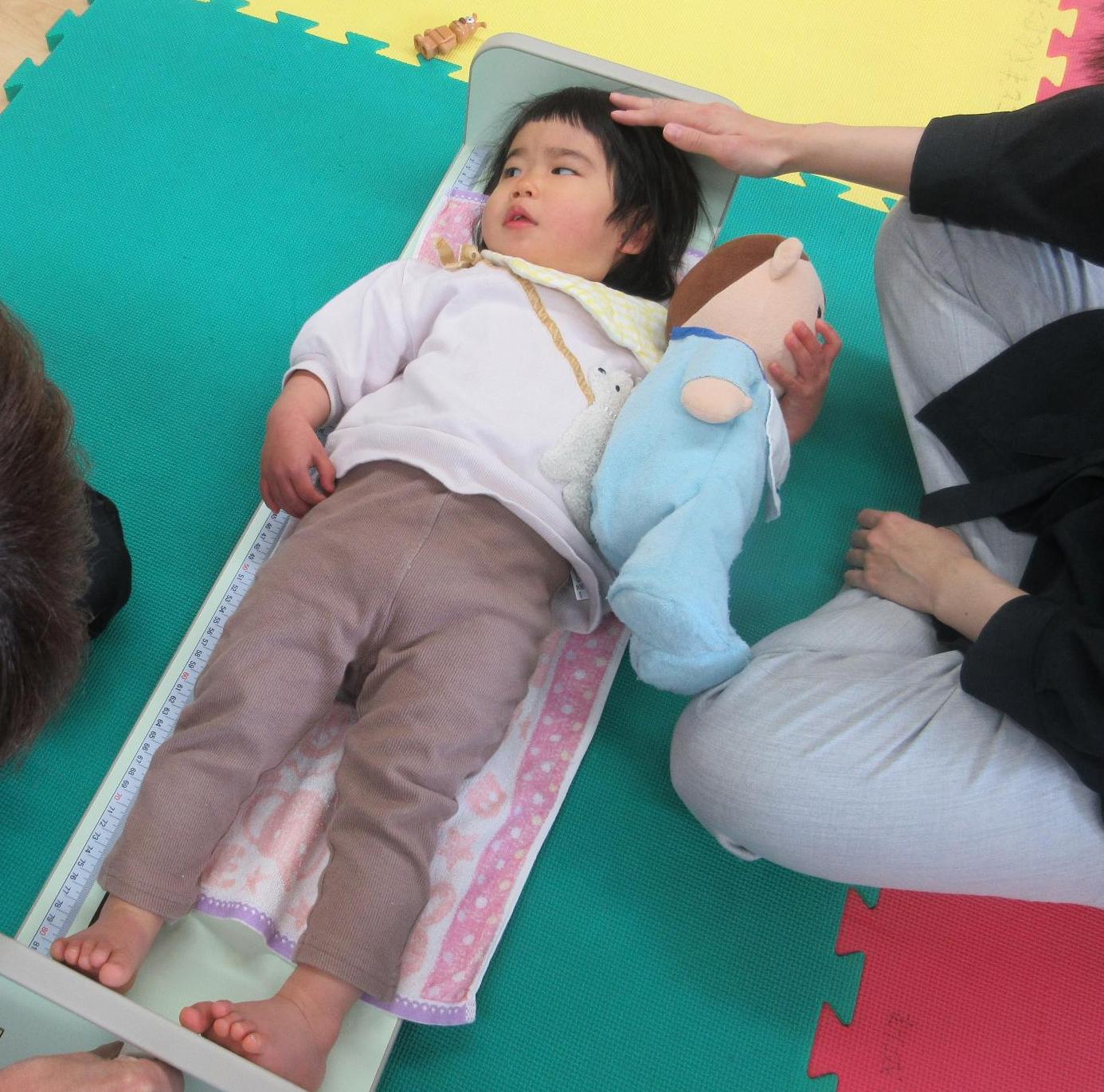 お気に入りの赤ちゃんのお人形のそらくんを抱えて身長測定台に落ち着いて寝る幼児さん