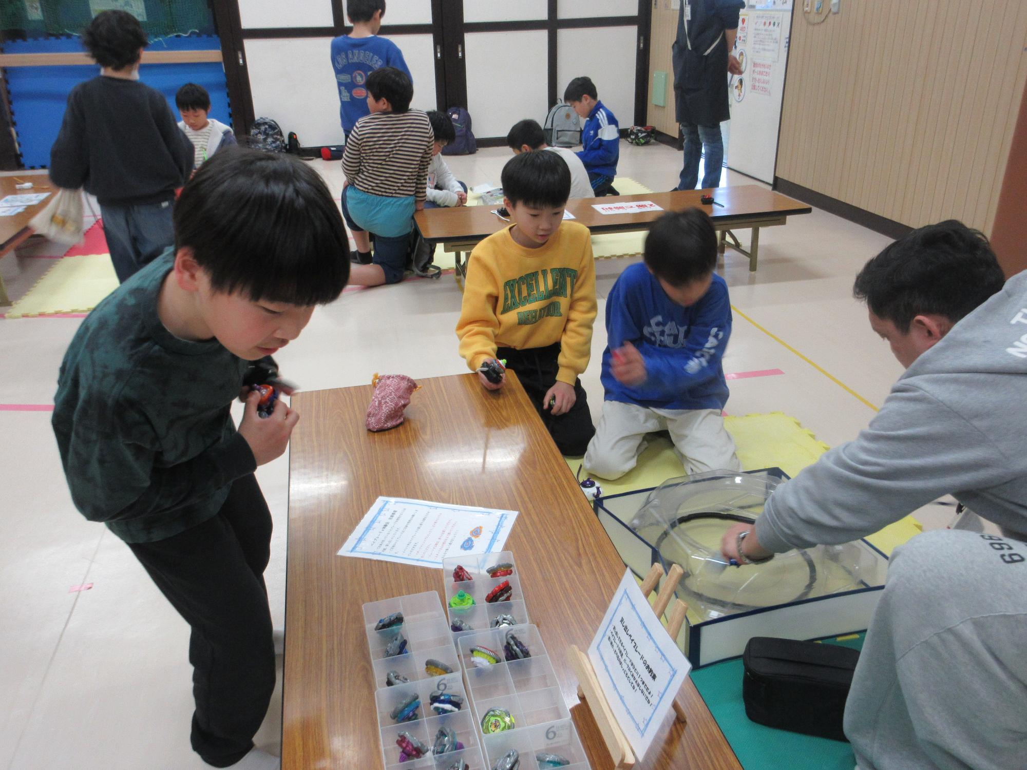 講師の持参したベイブレードを眺める子どもと講師とバトルをする子どもたち