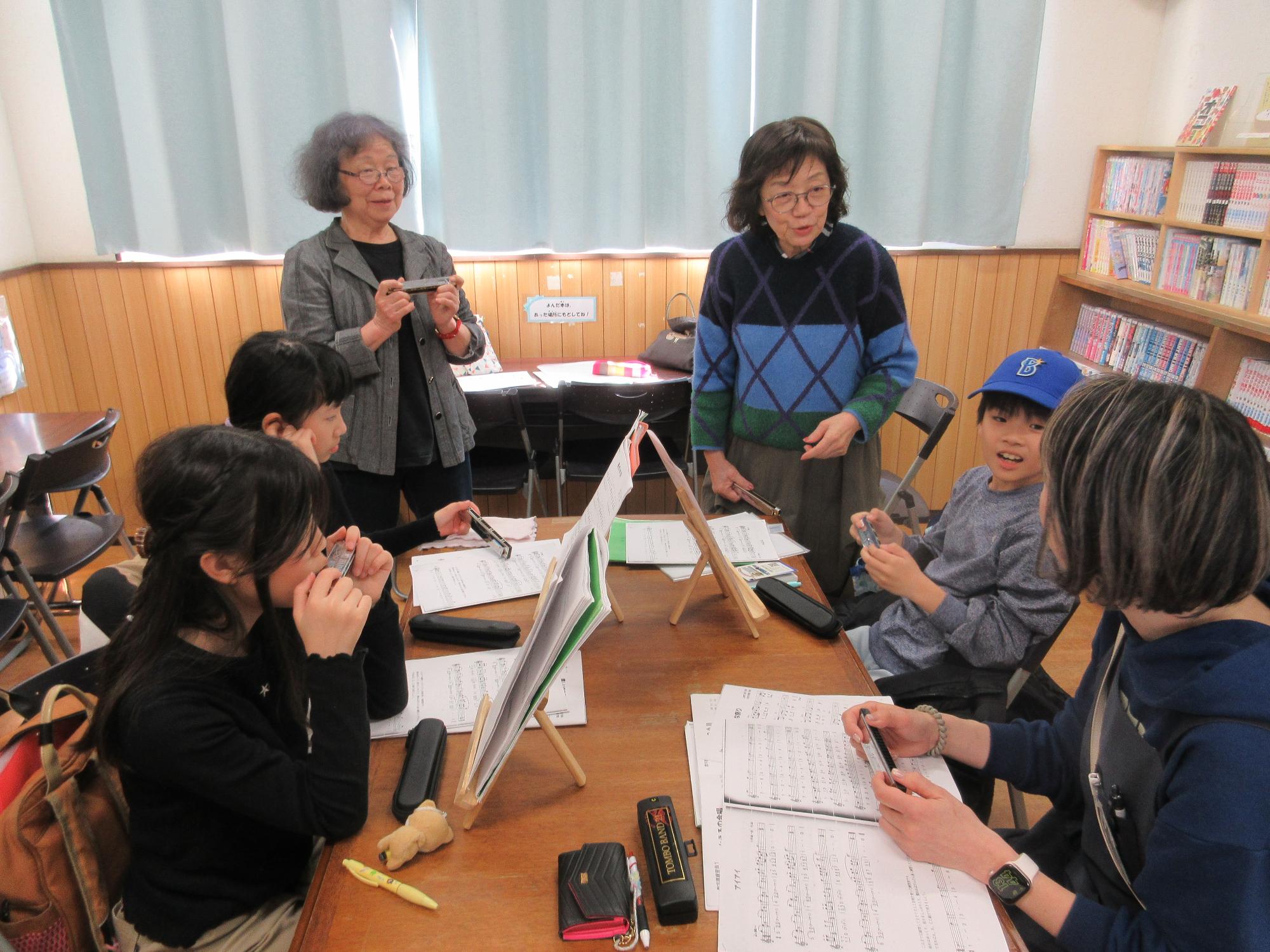 2人の講師と生徒3名がテーブルに楽譜を広げて練習しているところ