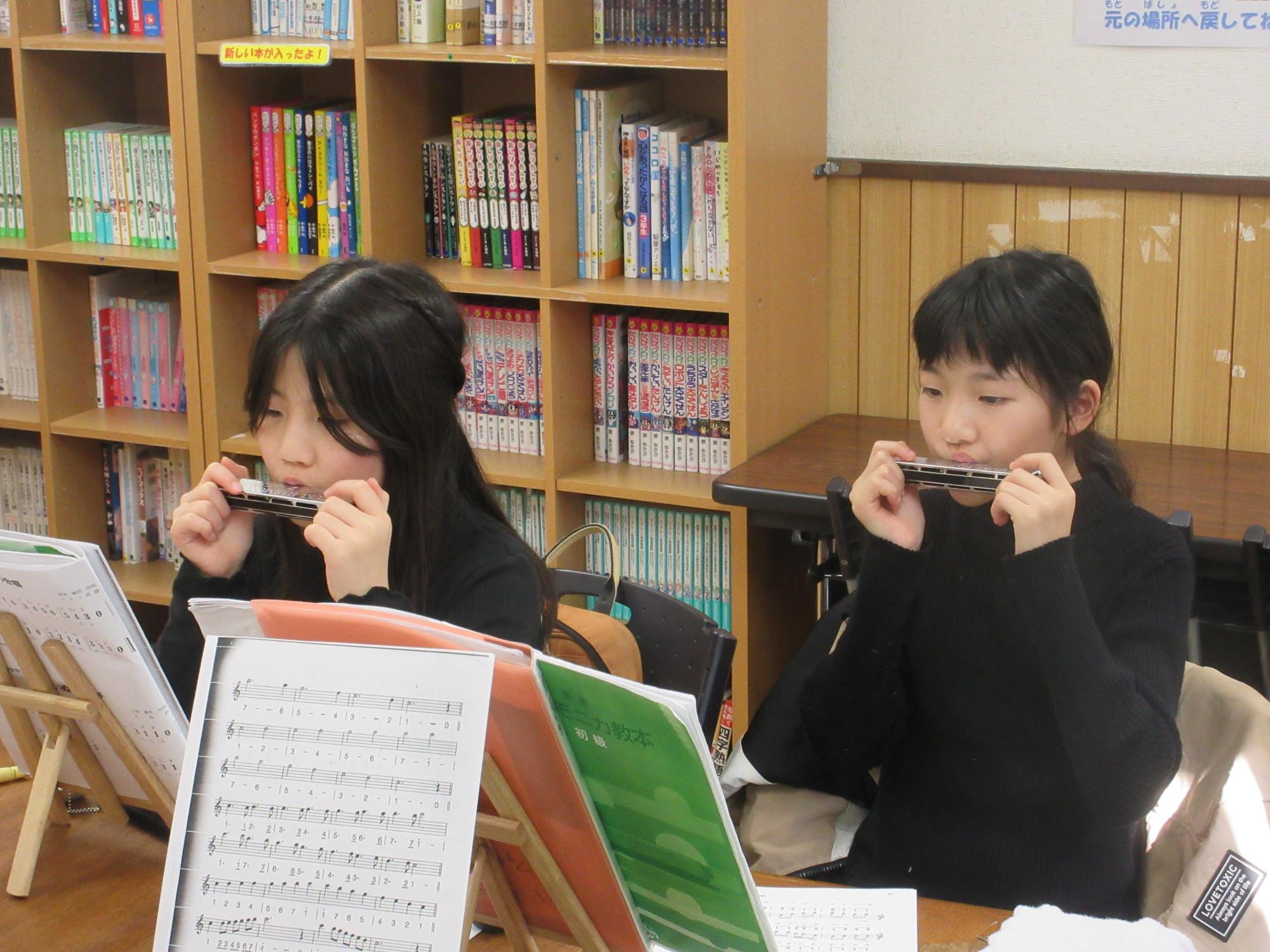 楽譜を見つめハーモニカを吹く二人の子ども