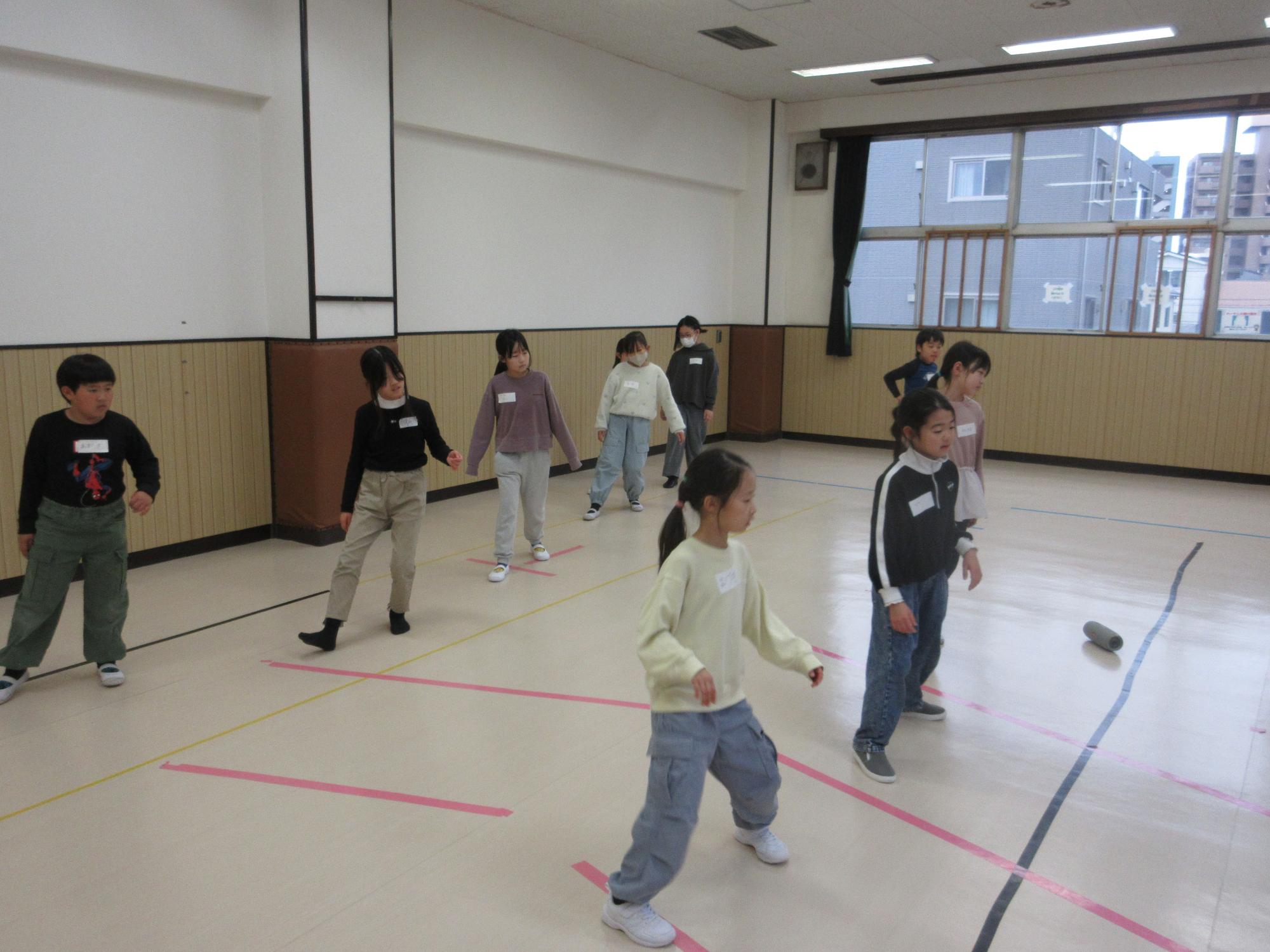 二列に並び右足かかとを横に出し重心は後ろにかけて顔は正面に向けるステップをする子どもたち