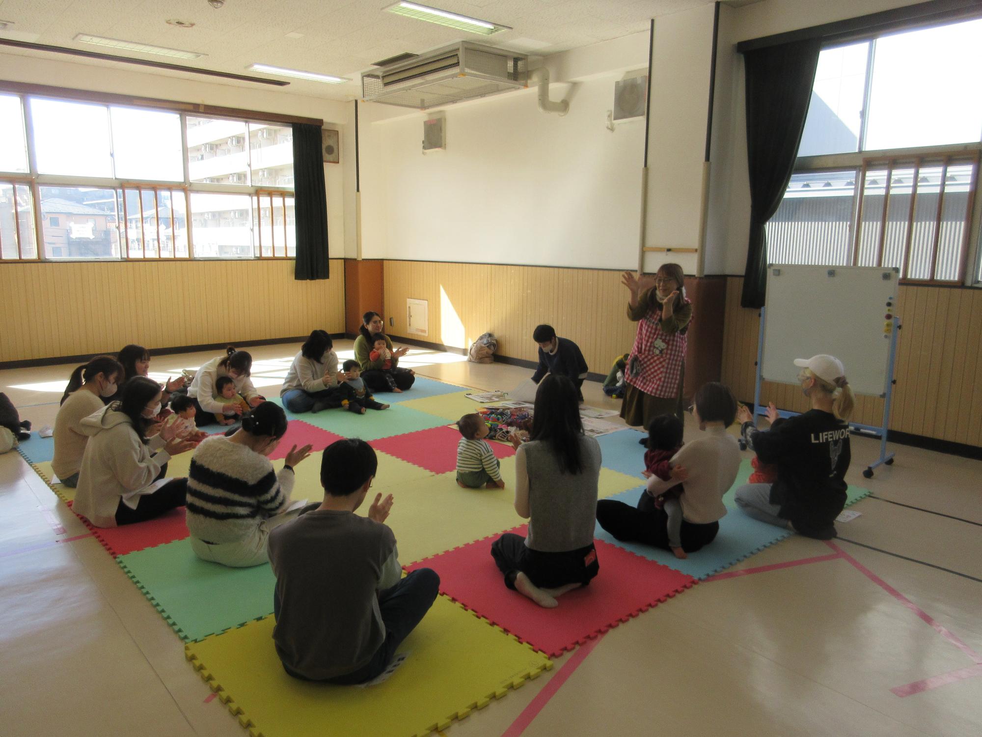 マットに円になって親子で座りいしちゃんと手遊びをしているところ