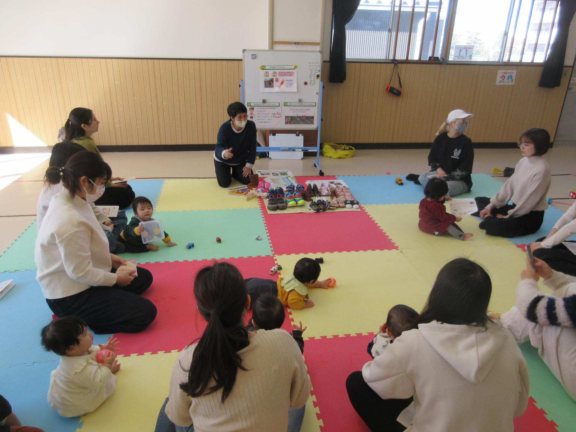 デザインの異なる靴をたくさん並べて靴の選び方を説明する講師と話を聞く親子